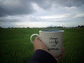 Person holding white cup of coffee or tea in hand with text message - Change your life with gratitude. On gray blue sky over field Royalty Free Stock Photo