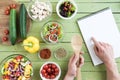 Person holding wooden spoon and pointing at recipe in cookbook while cooking