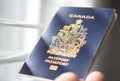 A person holds a Canadian passport next to a window
