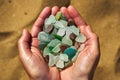 A person holds a collection of multi colored sea glass in their cupped hands with the sand in the background