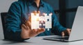 Person holding glowing puzzle pieces while using a laptop computer on a white desk surface top Royalty Free Stock Photo