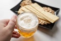 Person holds a mug of unfiltered light wheat beer, beer snacks on white table Royalty Free Stock Photo