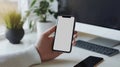 Person holding smartphone with blank screen near computer in modern workspace Royalty Free Stock Photo