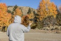 Person in hoodie sweatshirt catches flying drone in front of autumn leaf background