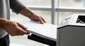 Individual placing blank sheets of paper into a printer, showcasing the printing process in a modern office environment with Royalty Free Stock Photo