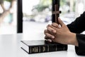 A person interlacing his hands on the book of the Bible and holding a cross, he is praying to the Bible, he reads and studies the