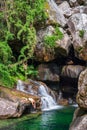 Person jumping into the emerald green lake under the waterfalls