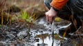 A person kneeling next to a shallow bog using a sharp tool to through the wet peat