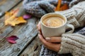 Person in knitted sweater holding a mug of frothy coffee, symbolizing comfort and warmth in autumn