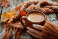 Person in knitted sweater holding a mug of frothy coffee, symbolizing comfort and warmth in autumn