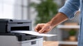 Individual with light skin tone is retrieving printed document from modern printer in bright office environment, showcasing Royalty Free Stock Photo