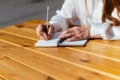 Person makes notes with a pencil in a notebook while sitting in a cafe in the summer on the street