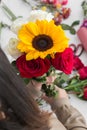 Person making with her hands a flower bouquett with sunflower, roses in the background work space Royalty Free Stock Photo