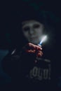 Person in a mask holding a lit lighter near the camera with blurred background in a dark room Royalty Free Stock Photo