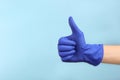 Person in medical gloves showing thumb up on light blue background, closeup of hand. Space for text Royalty Free Stock Photo