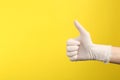 Person in medical gloves showing thumb up on yellow background, closeup of hand. Space for text Royalty Free Stock Photo