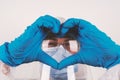 Person with medical hygienic protection glasses and blue gloves is looking through fingers formed to a heart