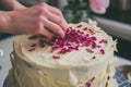 person meticulously adding candied rose petals to an icingcovered cake