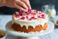 person meticulously adding candied rose petals to an icingcovered cake