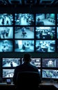 Person monitors multiple screens showing surveillance footage. Security operator observes real-time data. Modern control room