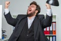 Person in an office bursts out in jubilation and pulls his arms up in the air