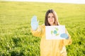 Person in overalls holds paper with a call to save the planet while standing on green field on sunset and the other hand shows a Royalty Free Stock Photo