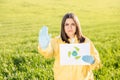 Person in overalls holds paper with a call to save the planet while standing on green field on sunset and the other hand shows a Royalty Free Stock Photo