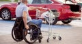Person with a physical disability pushes a cart towards a car in a supermarket parking lot Royalty Free Stock Photo