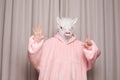 Person in pink hoodie with lama head showing gestures on studio wall background