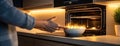 A person places a bowl of colorful dishes into a sleek oven in a contemporary kitchen, showcasing an inviting cooking
