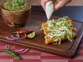 Person placing cream of milk on golden tacos with chicken typical Mexican food