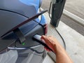 A person plugging in a gray Tesla to a charging station