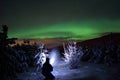 Person pointing flashlight beam towards aurora borealis on winter night sky in spruce tree field