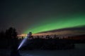 Person pointing flashlight beam towards aurora borealis on winter night sky