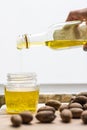 Person pour gourmet nut oil in a jar and nuts are on a wooden table