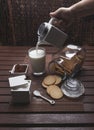 Person pouring milk into the glass on a rustic wooden table with cookies, sugar, and cinnamon powder