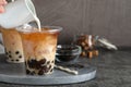 Person pouring milk into plastic cup with tea at grey table, closeup. Space for text