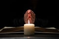 Person Praying with Hands Over Bible Illuminated by Candle Light Royalty Free Stock Photo