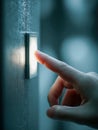 Person pressing a glowing button on a textured wall in a dimly lit indoor environment symbolizing decision or activation concept Royalty Free Stock Photo