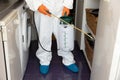 Person in protective suit with decontamination sprayer bottle disinfecting kitchen. COVID-19 pandemic concept