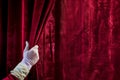 person pulling open red velvet curtain with white gloved hand Royalty Free Stock Photo