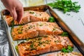 person pulling out a tray of baked salmon fillets, herbs on top