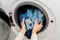 Person putting jeans into the drum of a washing machine, front view.