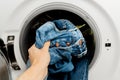 Person putting jeans into the drum of a washing machine, front view. Washing dirty jeans