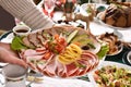 A Person Putting A Platter With Sliced Ham And Cured Meats On Christmas Eve Table