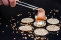 Person putting salmon with sticks on crackers with cream cheese