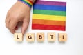 Person with a rainbow bracelet forming with wood the word LGBTI next to the rainbow flag on a white background