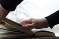 A person reading books near the window. Hands turns over book page