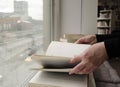 A person reading books near the window. Hands turns over book page