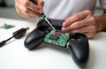 Person repairs broken gamepad controller with screwdriver at white desk. Tech expert fixes electronic device at home. Man does Royalty Free Stock Photo